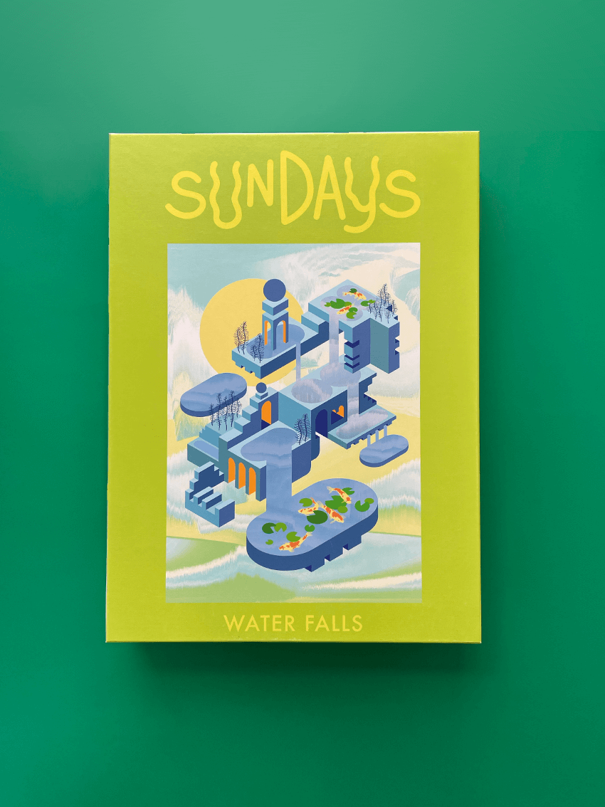 Auf grünem Hintergrund liegt eine hellgrüne Box mit der Aufschrift "Sundays" und "Water Falls" und dem Bild des fertigen Puzzles. Das Bild zeigt eine Landschaft aus surrealer blauer Architektur mit Bäumen und kleinen Teichen mit Kois.