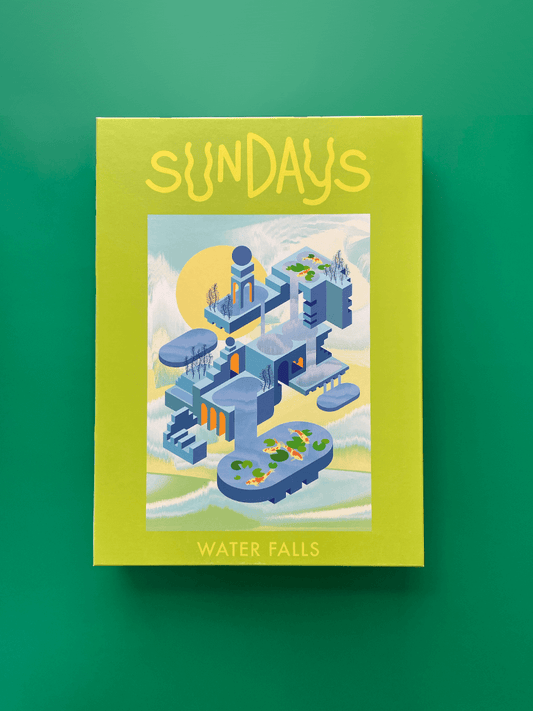 Auf grünem Hintergrund liegt eine hellgrüne Box mit der Aufschrift "Sundays" und "Water Falls" und dem Bild des fertigen Puzzles. Das Bild zeigt eine Landschaft aus surrealer blauer Architektur mit Bäumen und kleinen Teichen mit Kois.
